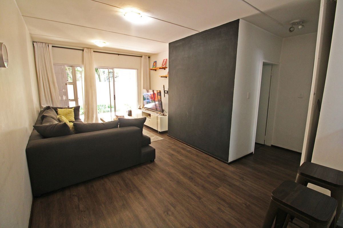 A well-lit living room featuring dark laminate flooring, a prominent accent wall, and sliding glass doors providing access to the outdoor area.
