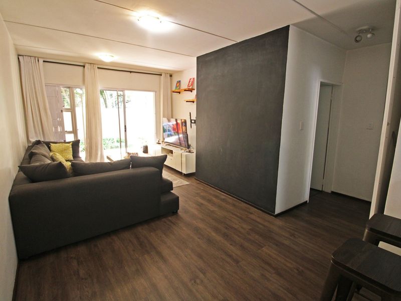 A well-lit living room featuring dark laminate flooring, a prominent accent wall, and sliding glass doors providing access to the outdoor area.