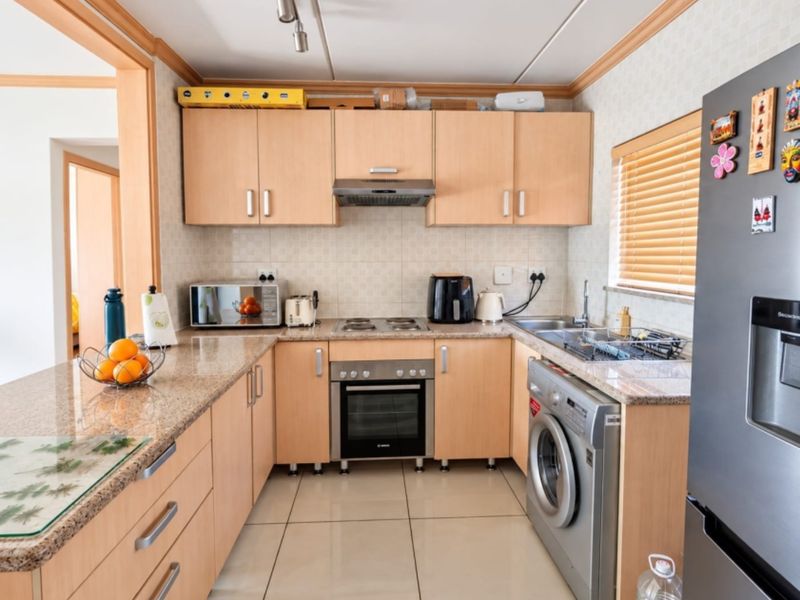 A functional kitchen featuring light wood cabinetry, granite countertops, a built-in oven with hob, and integrated laundry facilities with tiled flooring.