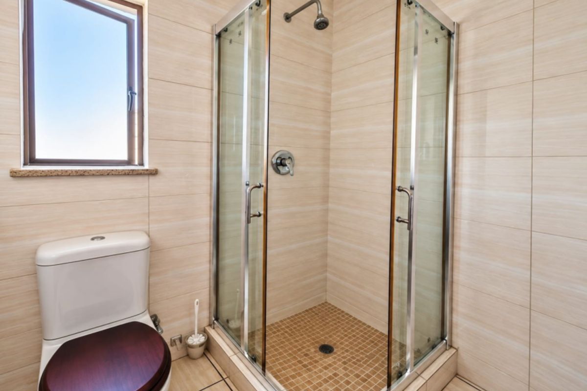 A clean bathroom featuring a glass-enclosed shower, tiled walls and flooring, and a standard toilet with a window for natural light.
