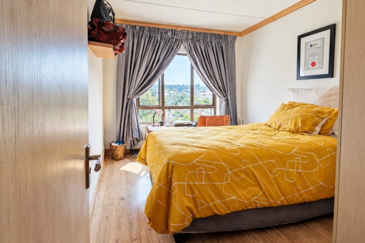 A well-lit bedroom featuring laminate flooring, a large window with natural light, and neutral wall finishes.