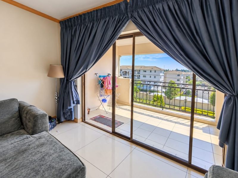 Bright living area featuring large sliding glass doors that open onto a private balcony with neighborhood views and tiled flooring throughout.