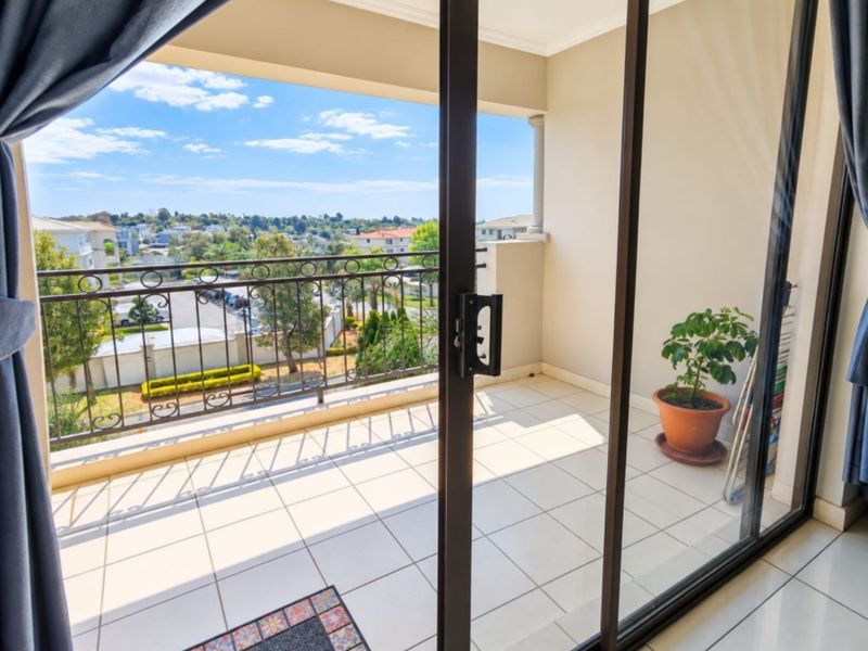 A bright, tiled balcony featuring a wrought iron balustrade and sliding glass door access, offering elevated views of the surrounding neighborhood.