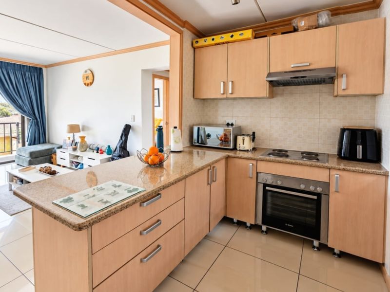 Open-plan kitchen featuring light wood cabinetry, granite countertops, and integrated appliances, flowing seamlessly into the adjacent living area.