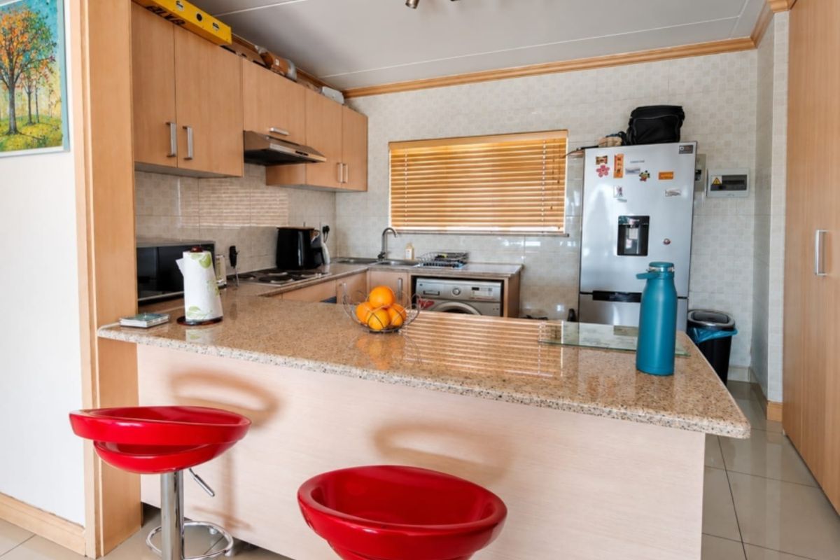 A functional kitchen featuring granite countertops, light wood cabinetry, and tiled flooring, offering a practical layout with integrated appliances and breakfast bar seating.