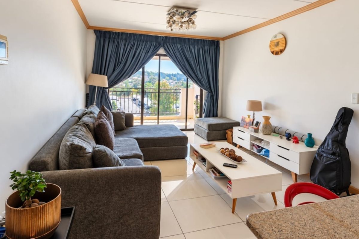 A bright living room featuring large format floor tiles, coving, and a sliding glass door providing access to a balcony with an outdoor view.