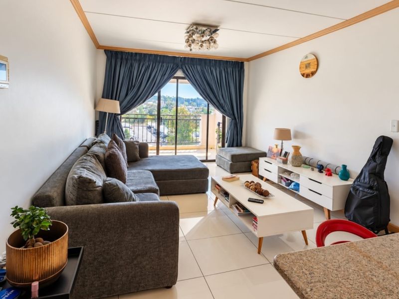 A bright living room featuring large format floor tiles, coving, and a sliding glass door providing access to a balcony with an outdoor view.