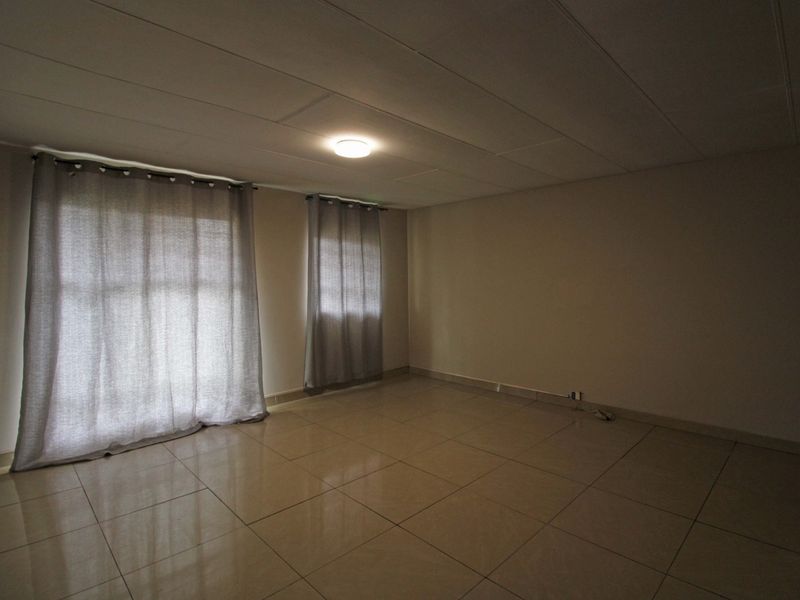 A spacious, empty living area featuring neutral tiled flooring and a simple ceiling finish, ready for personalization.