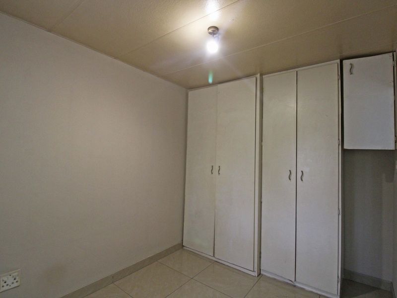 A vacant bedroom featuring tiled flooring and built-in storage cupboards, offering a blank canvas for potential interior updates.
