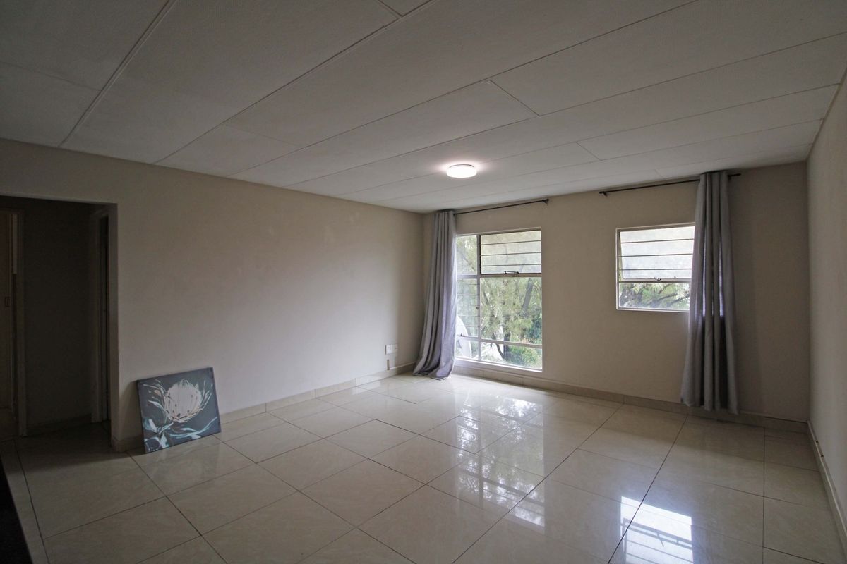 A spacious, empty living area featuring polished tile flooring, neutral walls, and large windows that provide natural light.