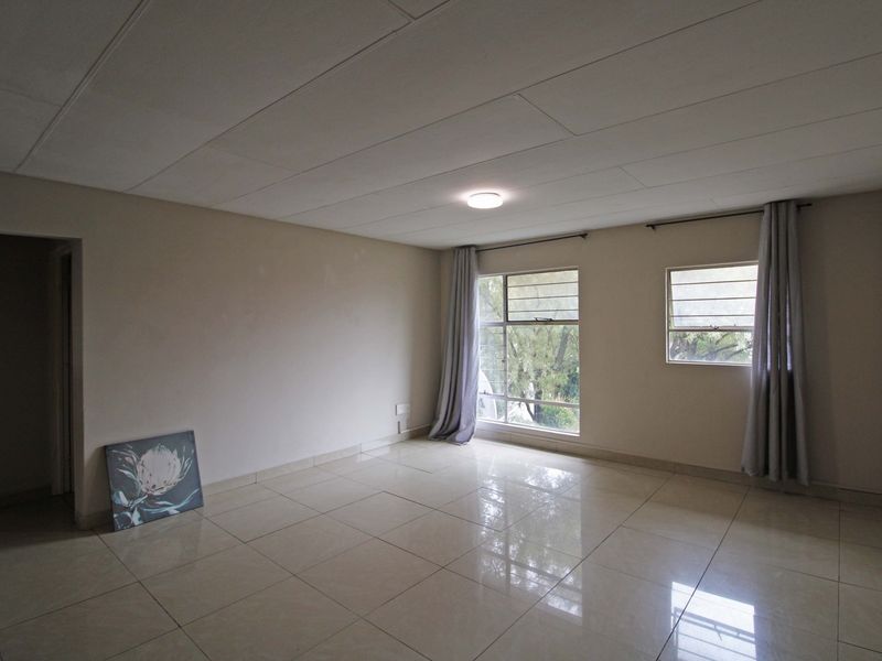 A spacious, empty living area featuring polished tile flooring, neutral walls, and large windows that provide natural light.