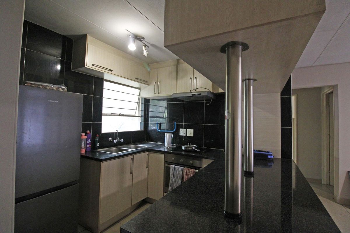 Compact kitchen featuring dark granite countertops, light wood cabinetry, a breakfast bar, and a tiled backsplash with integrated oven and extractor fan.