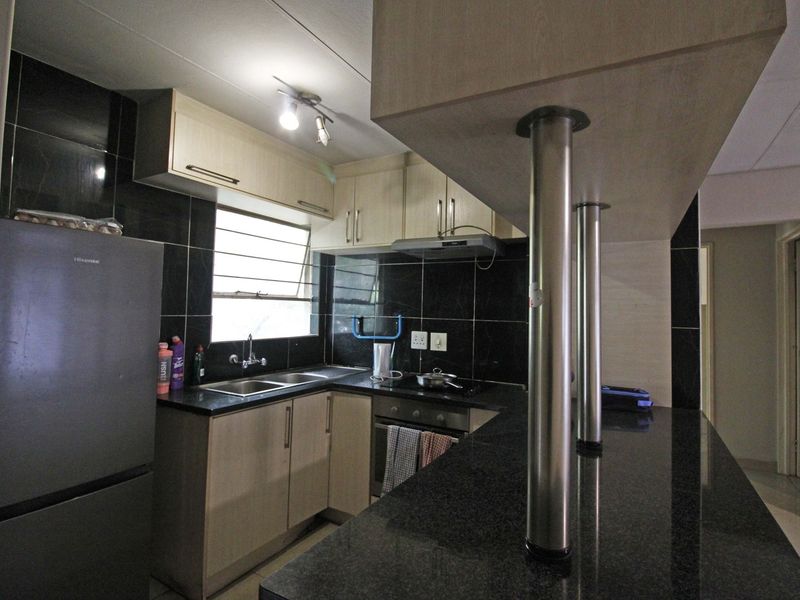 Compact kitchen featuring dark granite countertops, light wood cabinetry, a breakfast bar, and a tiled backsplash with integrated oven and extractor fan.