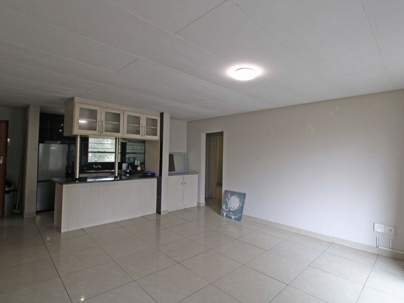 An open-plan living and kitchen area featuring neutral tiled flooring, built-in kitchen cabinetry with an island, and a clean, minimalist layout.