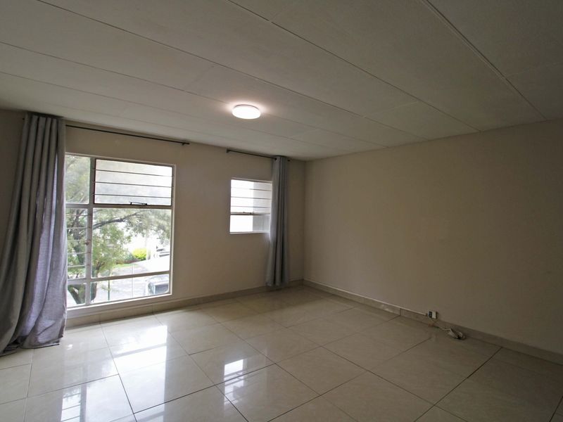 A spacious, empty living area featuring neutral tiled flooring, large windows providing natural light, and a clean, minimalist aesthetic ready for personalization.