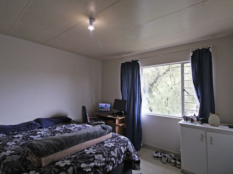 A functional bedroom featuring tiled flooring, a large window providing natural light, and a standard ceiling light fixture.