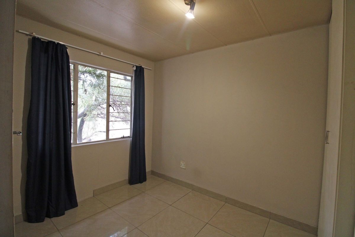A clean, empty bedroom featuring neutral tiled flooring, a built-in cupboard, and a window with natural light.