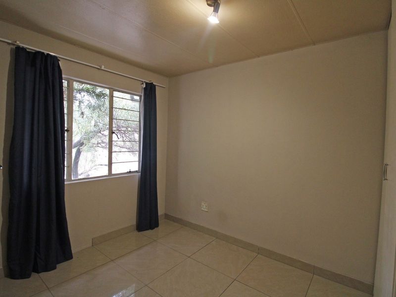 A clean, empty bedroom featuring neutral tiled flooring, a built-in cupboard, and a window with natural light.
