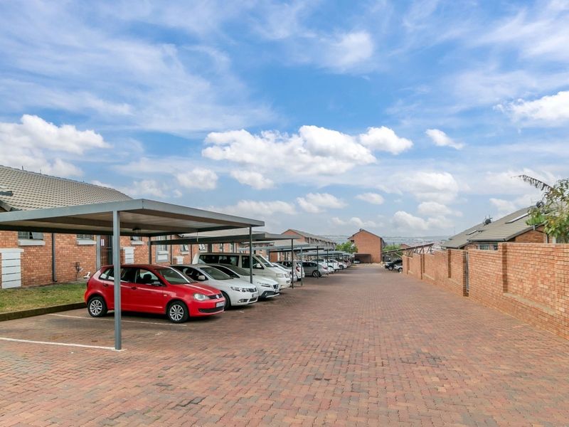 Exterior view of the apartment complex featuring paved parking area with covered carports and face brick building facades.