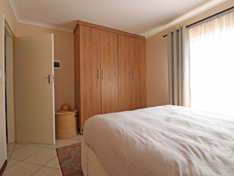 A well-maintained bedroom featuring neutral walls, tiled flooring, and a large built-in wooden wardrobe providing ample storage space.