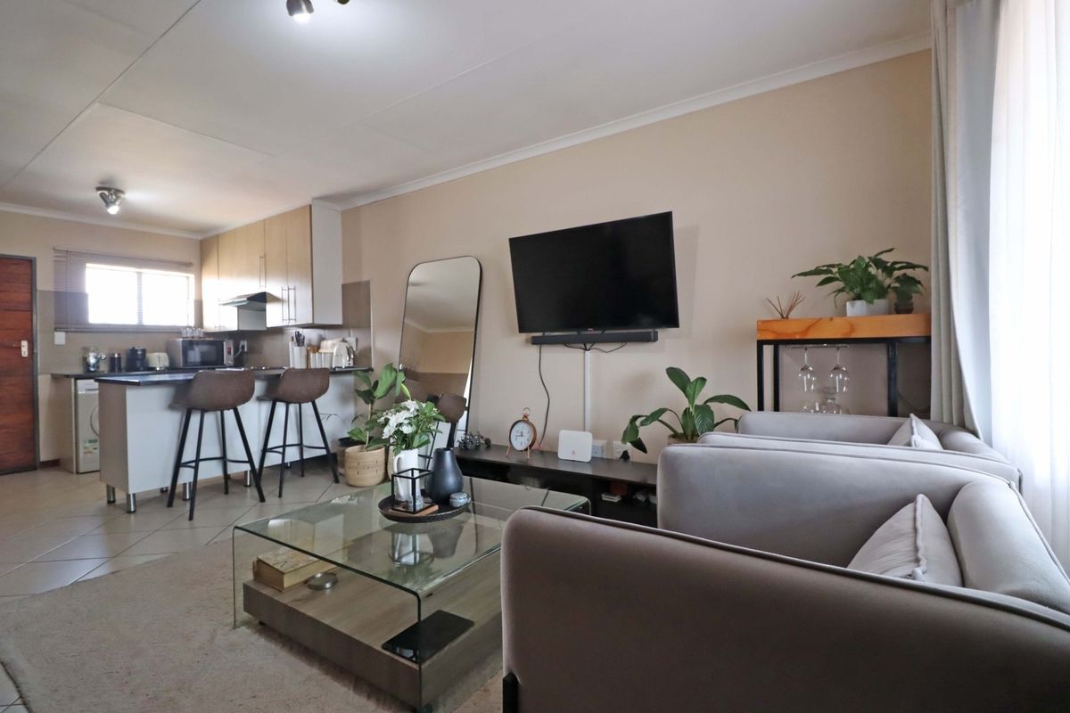 An open-plan living area featuring a modern kitchen with island seating, tiled floors, and neutral wall finishes, creating a functional and cohesive living space.