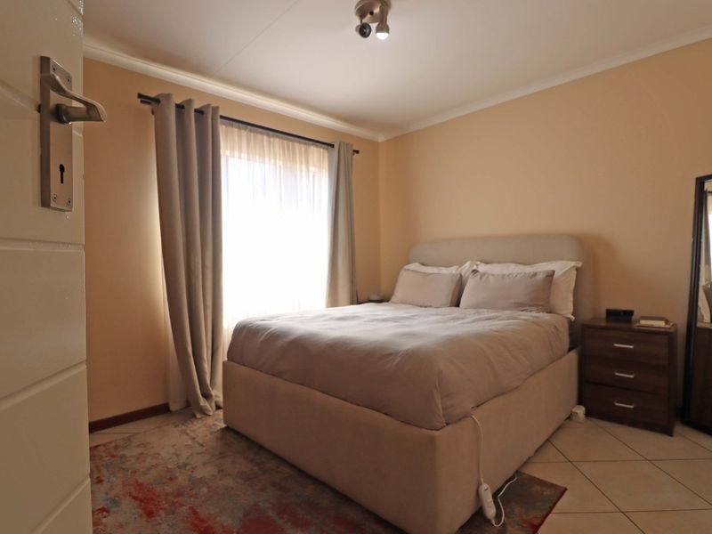 A functional bedroom featuring tiled flooring, neutral wall tones, and a window with curtain treatments, providing a comfortable and well-lit sleeping space.