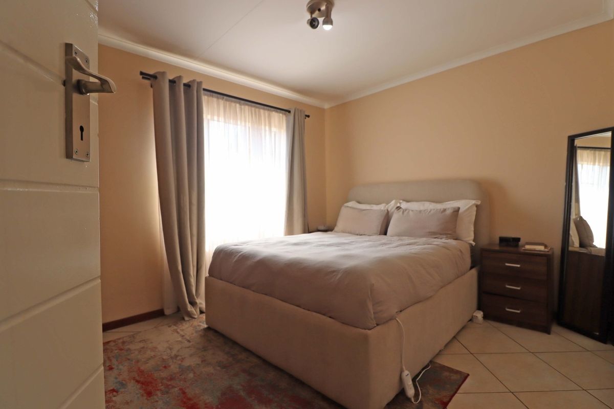 A functional bedroom featuring tiled flooring, neutral wall tones, and a window with curtain treatments, providing a comfortable and well-lit sleeping space.