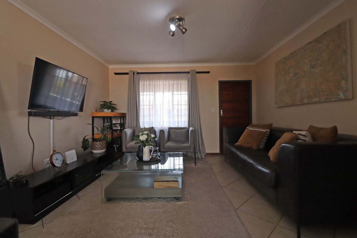 A comfortable living room featuring tiled flooring, neutral wall tones, and a ceiling-mounted spotlight fixture, providing a functional and well-lit space.