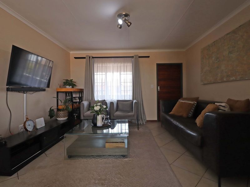 A comfortable living room featuring tiled flooring, neutral wall tones, and a ceiling-mounted spotlight fixture, providing a functional and well-lit space.