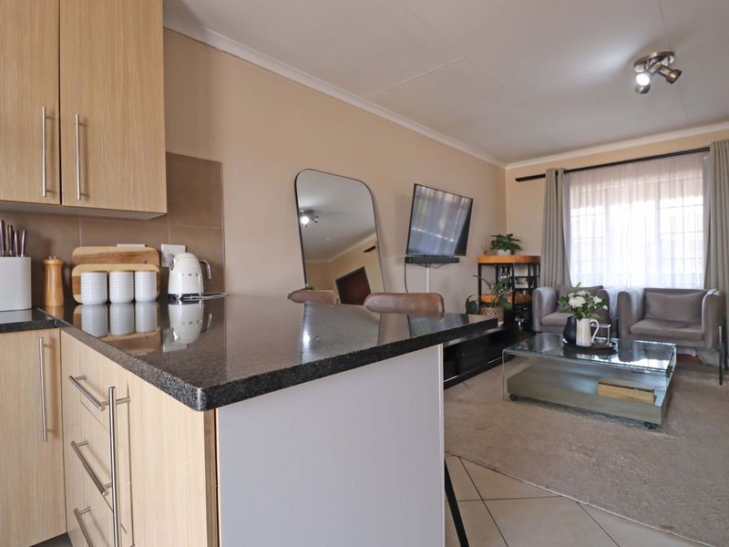 Open plan living area featuring a modern kitchen with laminate cabinetry and granite countertops, flowing into a comfortable lounge space with tiled flooring.