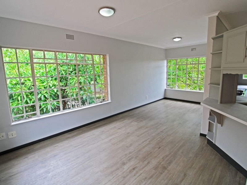 A bright and spacious open-plan living area featuring modern laminate flooring, neutral walls, and large windows providing ample natural light and garden views.