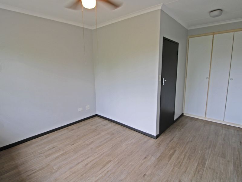 A clean, empty bedroom featuring modern laminate flooring, built-in cupboards, and a ceiling fan, offering a neutral canvas for personalization.