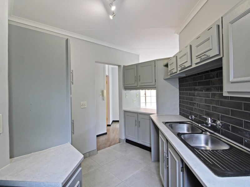 A clean, functional kitchen featuring grey cabinetry, a dark subway tile backsplash, double stainless steel sink, and neutral floor tiling.