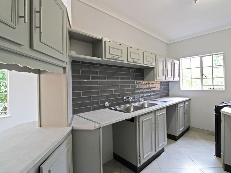A clean, functional kitchen featuring grey cabinetry, a modern subway tile backsplash, double stainless steel sink, and ample counter space.