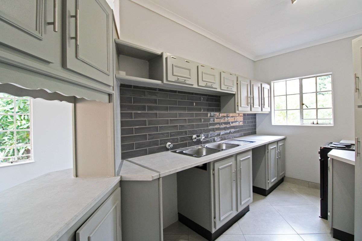 A clean, functional kitchen featuring grey cabinetry, a modern subway tile backsplash, double stainless steel sink, and ample counter space.