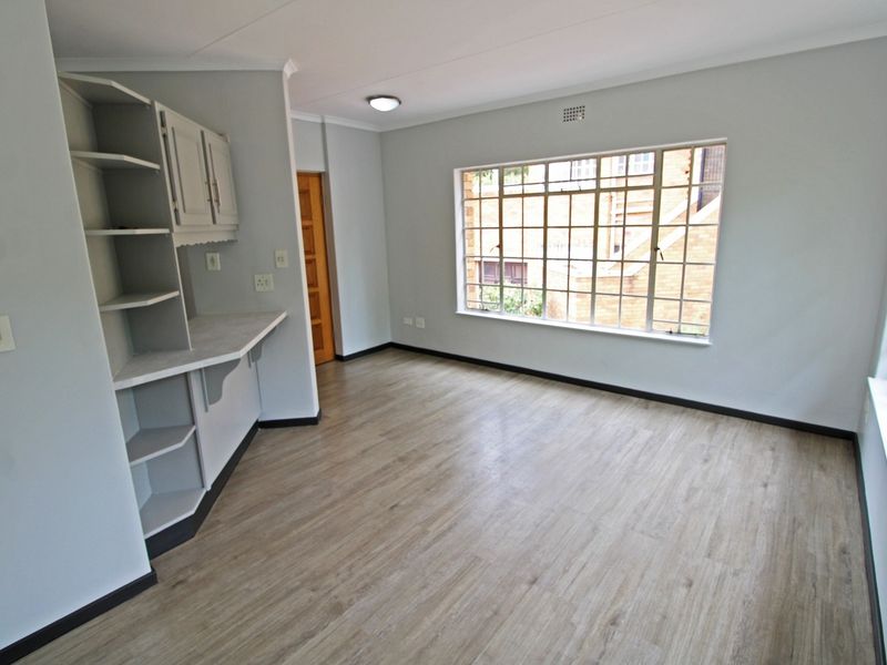 A bright, empty living area featuring modern laminate flooring, built-in shelving, and large windows that provide ample natural light.