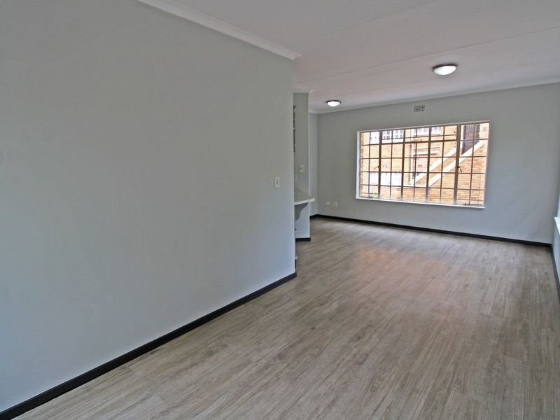 A bright, vacant open-plan living area featuring modern laminate flooring, neutral walls, and large windows providing ample natural light.