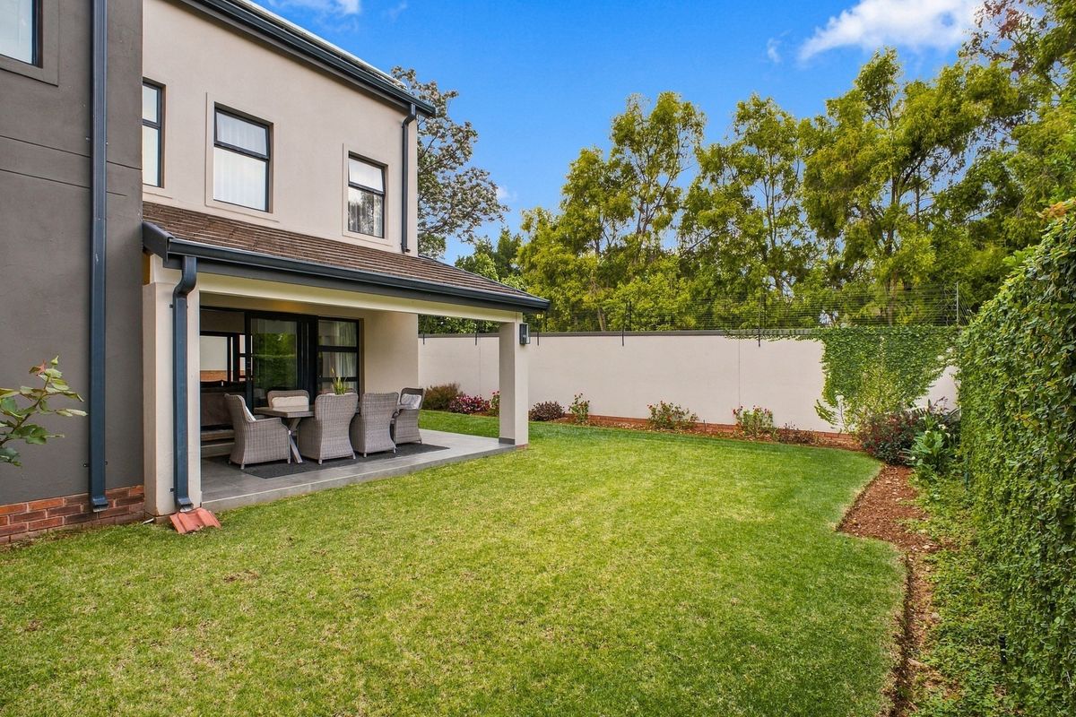 A well-maintained rear exterior featuring a covered patio with tiled flooring, a manicured lawn, and a secure perimeter wall with electric fencing.
