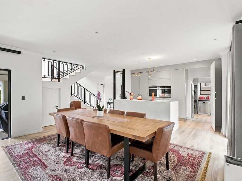 Spacious open-plan living and dining area featuring a modern kitchen with stone island, built-in appliances, and a staircase with decorative metal railing.