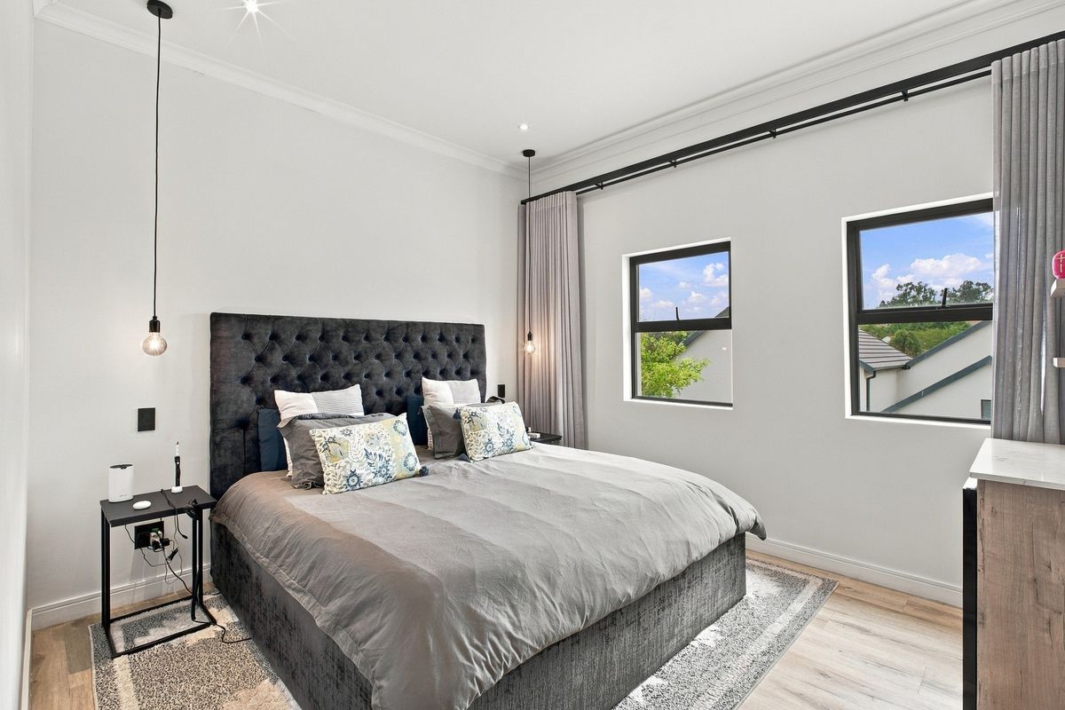 A modern, well-maintained bedroom featuring laminate flooring, recessed downlights, and large aluminium-framed windows with integrated curtain tracks.