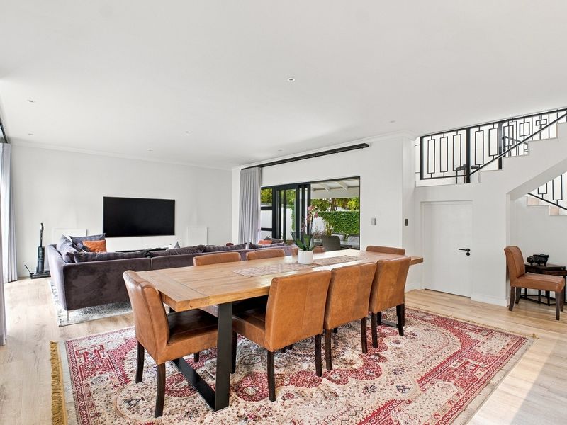 Spacious open-plan living and dining area featuring modern laminate flooring, recessed lighting, and a staircase with a decorative metal balustrade leading to upper levels.