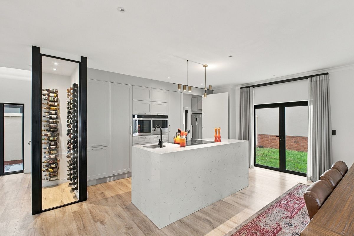 Modern kitchen featuring a central island with quartz countertops, integrated appliances, and a dedicated glass-enclosed wine storage area, opening onto a rear garden.