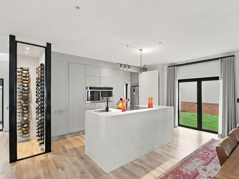 Modern kitchen featuring a central island with quartz countertops, integrated appliances, and a dedicated glass-enclosed wine storage area, opening onto a rear garden.