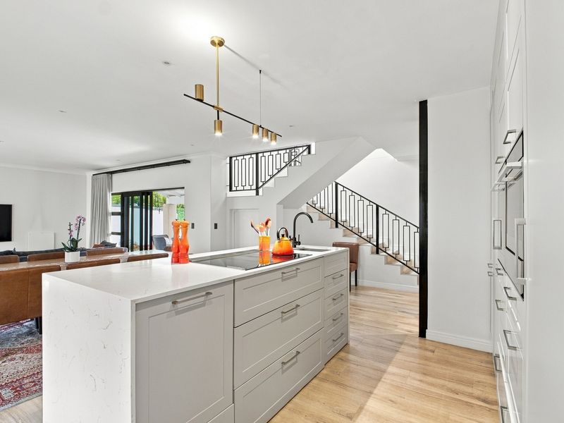 Modern open-plan kitchen featuring a central island with quartz countertops, integrated appliances, and a sleek staircase with a contemporary metal balustrade.