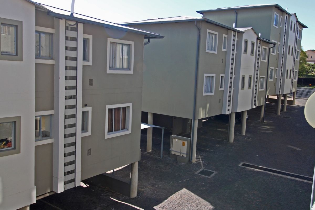 Exterior view of a multi-story apartment complex featuring stilted construction, paved ground-level parking, and modern facade finishes.