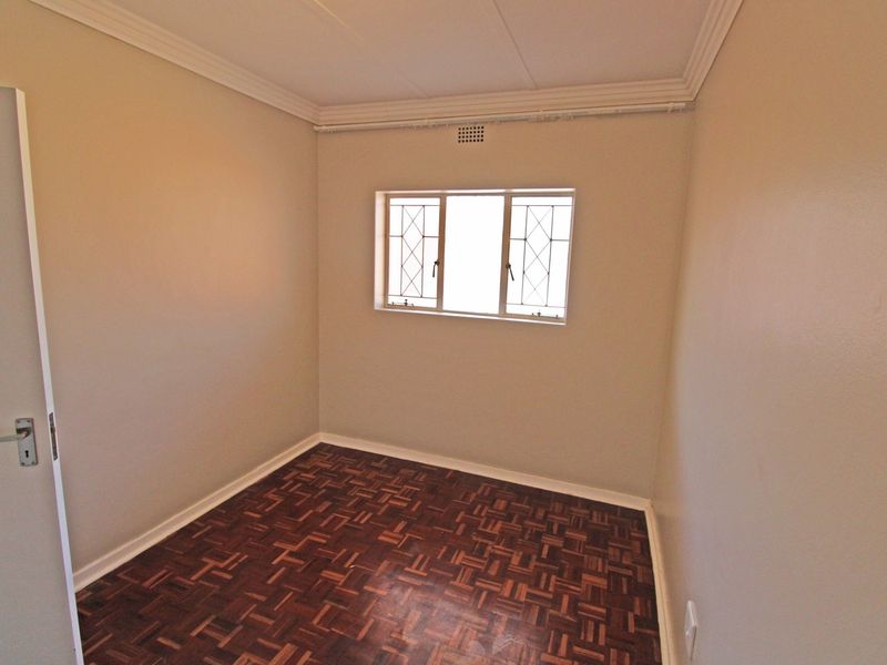 An empty bedroom featuring classic parquet flooring, neutral wall finishes, and a window fitted with security bars.