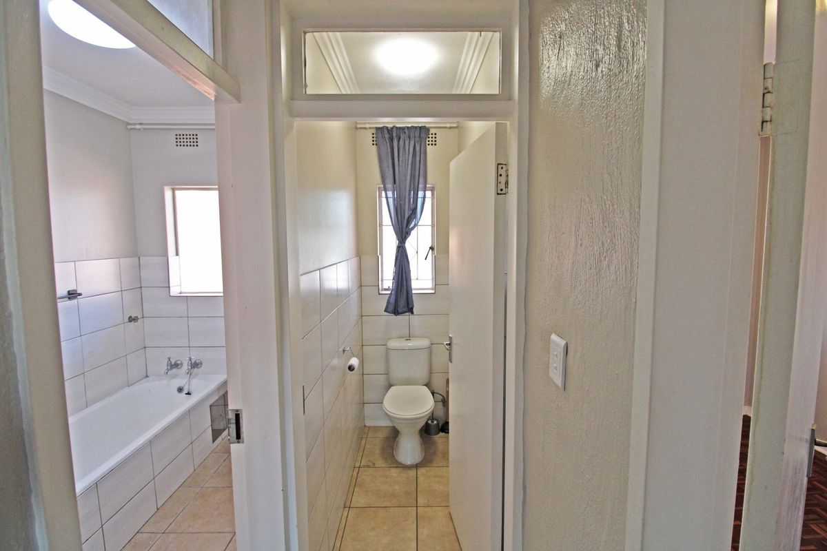 A functional bathroom featuring a bathtub and a separate toilet area with neutral ceramic tiling and transom windows for natural light.