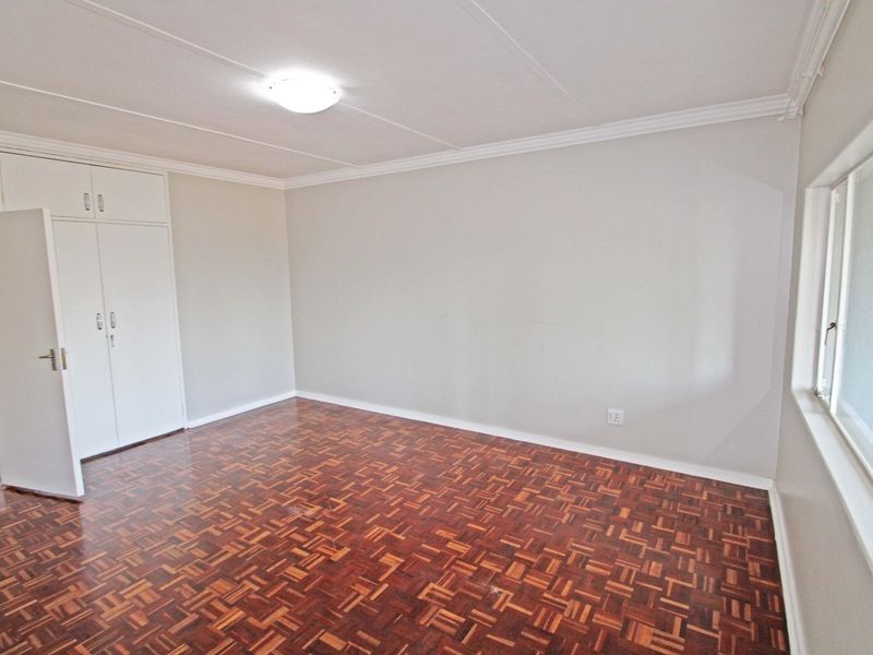 A bright, empty bedroom featuring classic parquet flooring, built-in cupboards, and neutral wall finishes, offering a clean canvas for personalization.