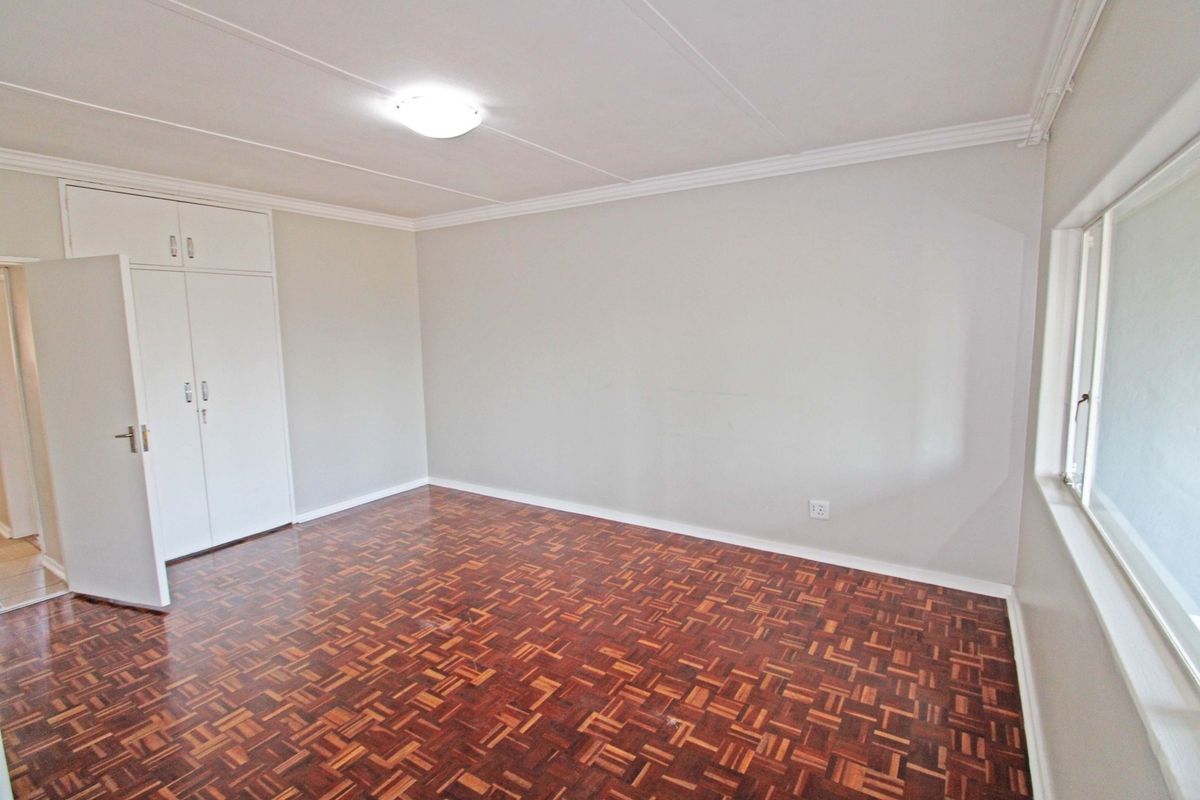 A bright, empty bedroom featuring classic parquet flooring, built-in cupboards, and neutral wall finishes, offering a clean canvas for personalization.