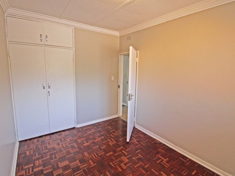 A vacant bedroom featuring classic parquet flooring, neutral wall tones, and built-in storage cupboards with overhead cabinetry.